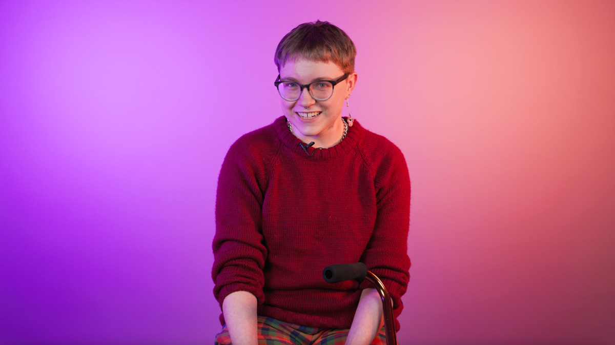 a young person looking off to the side and laughing, their cane resting on their arm 